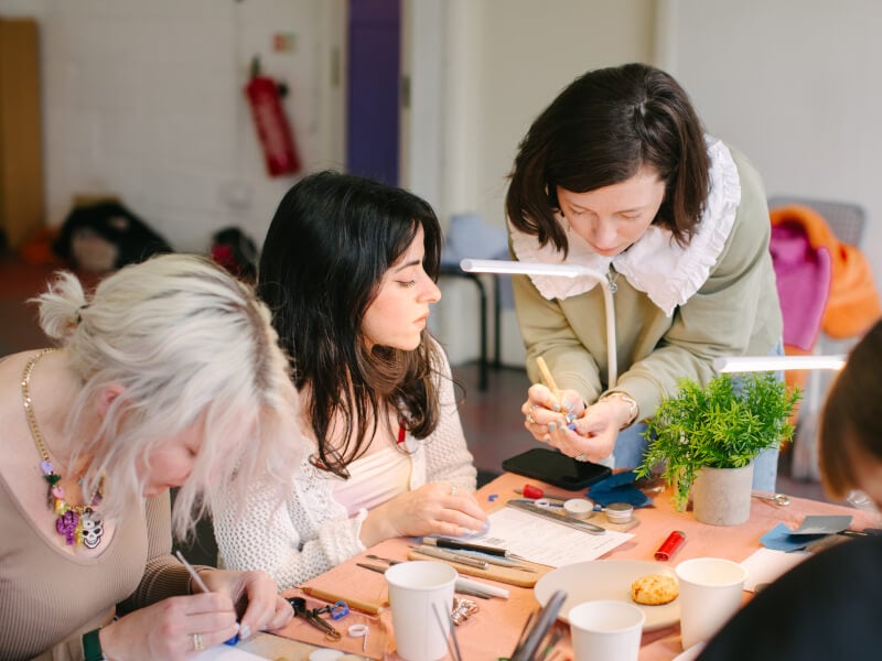 A jewellery making teacher is showing a student how to carve a wax mold